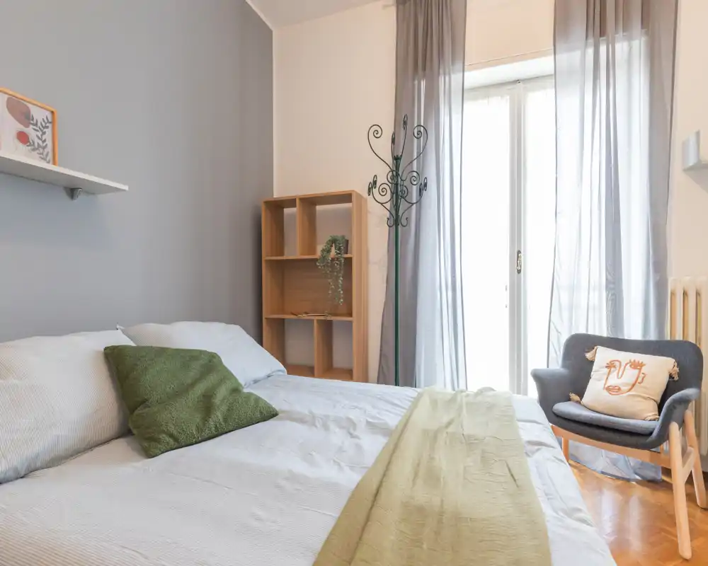 Camera da letto luminosa e accogliente con un ampio letto, biancheria morbida, una poltrona e luce naturale dalla porta-balcone.
