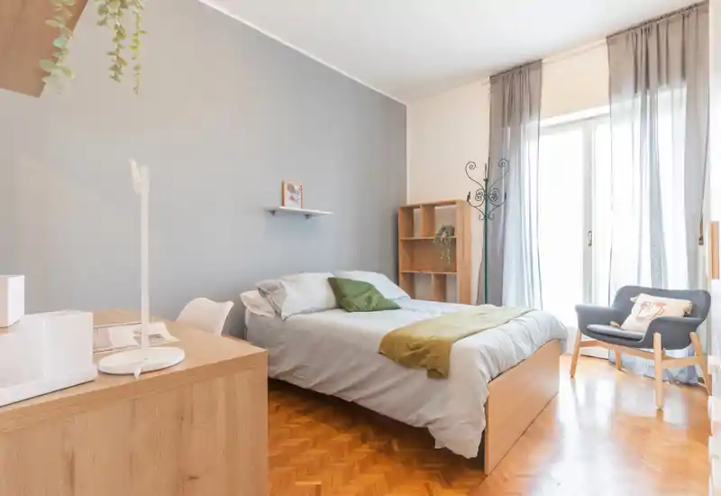 Bright, well-styled bedroom with a double bed, soft linens, a reading chair and natural light from floor-to-ceiling windows.