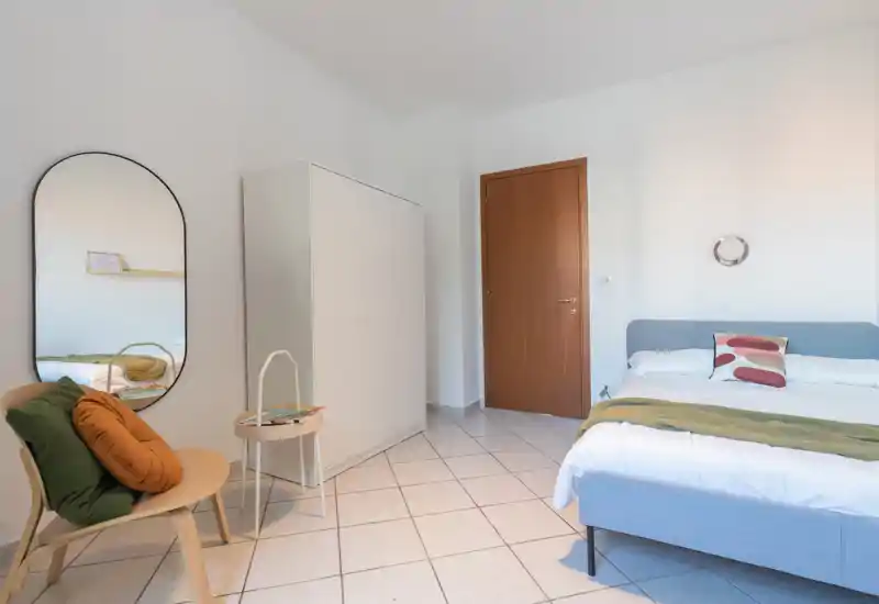Chambre lumineuse et soignée avec un lit double, coussins décoratifs, petit coin siège avec miroir et une armoire — parfaite pour un séjour confortable.