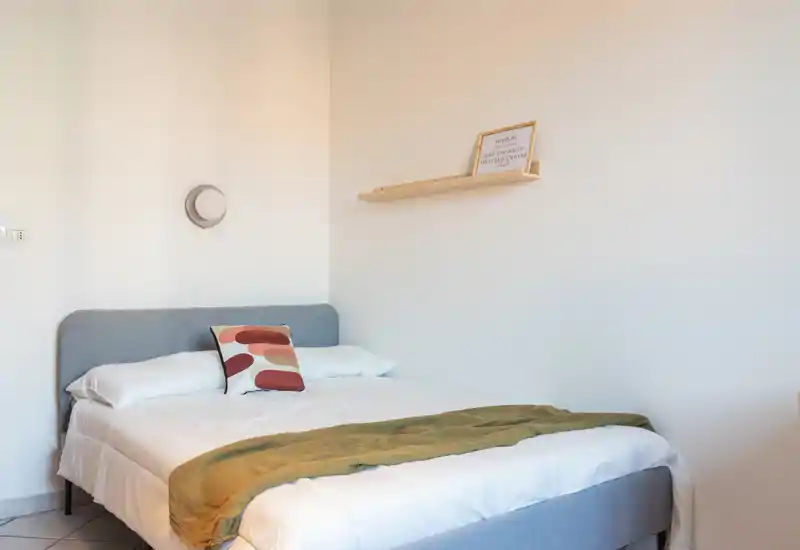Chambre lumineuse et minimaliste avec un lit double bien fait, un coussin décoratif et un plaid confortable.