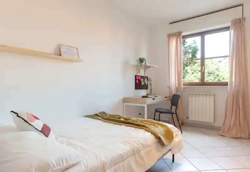 Chambre lumineuse et minimaliste avec un lit bien fait, des textiles doux et un petit bureau près de la fenêtre offrant une belle lumière naturelle.