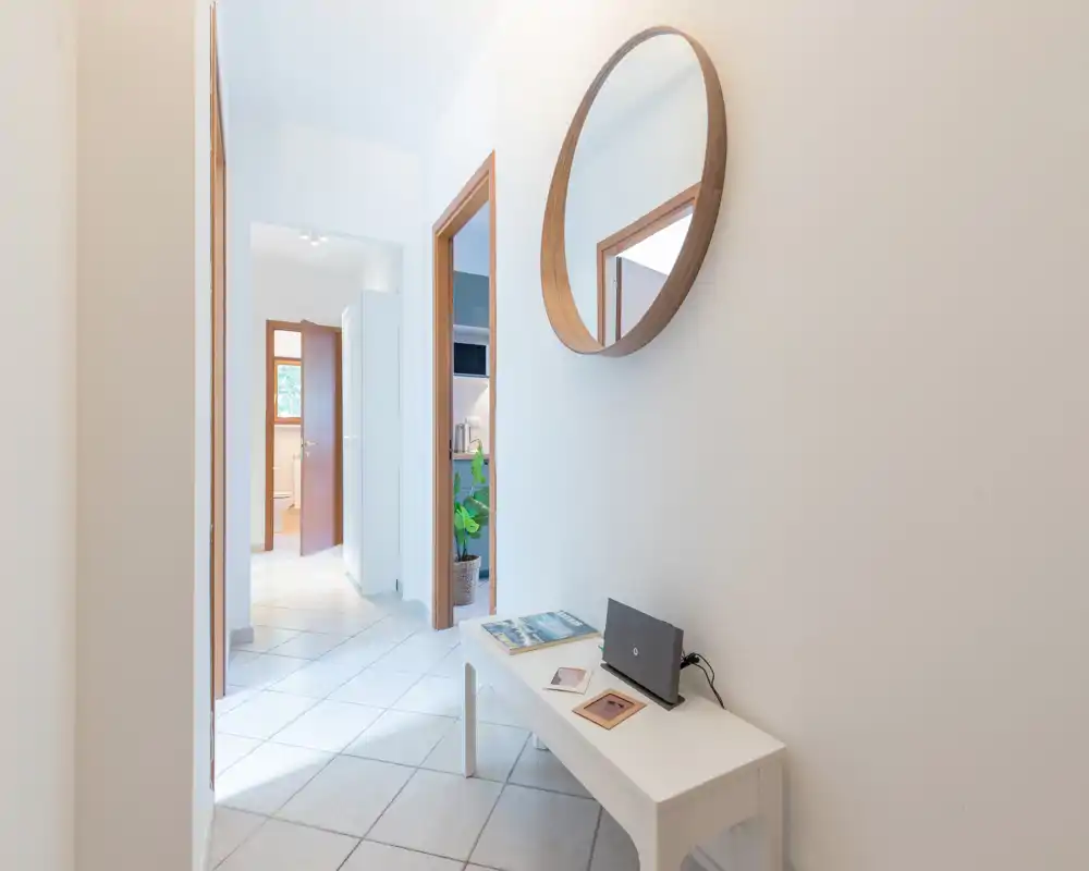 Entrée lumineuse et minimaliste avec un miroir rond, un petit banc et un sol carrelé — première impression propre et accueillante.