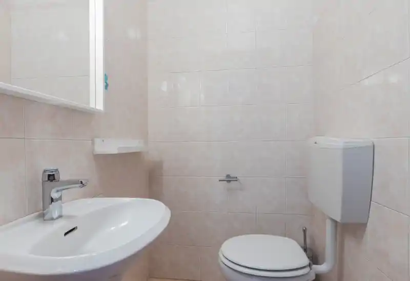 Clean, compact bathroom with wall-mounted cistern, toilet and a white sink; light-coloured tiled walls create a bright, neutral space.