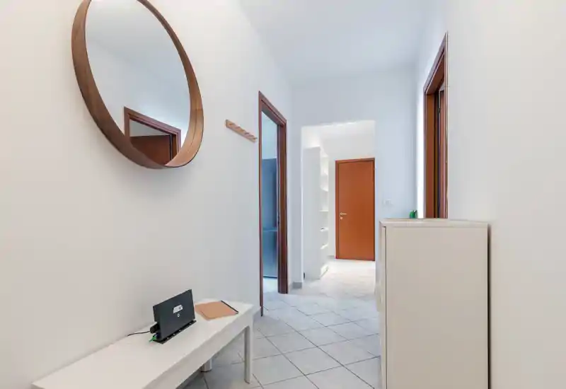 Bright, minimal entrance hallway with tiled floor, wall mirror, small bench and coat hooks — a clean, welcoming entry space.