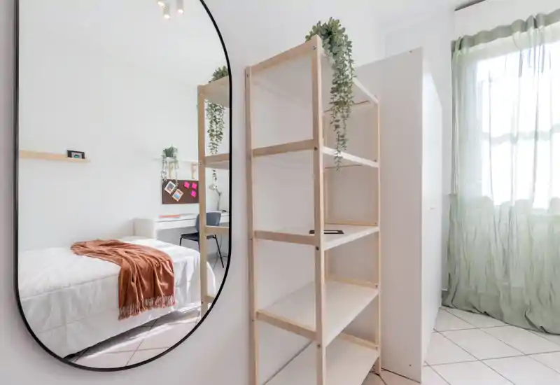 Chambre lumineuse et minimaliste avec lit blanc, plaid chaleureux et grand miroir décoratif qui agrandit l'espace.