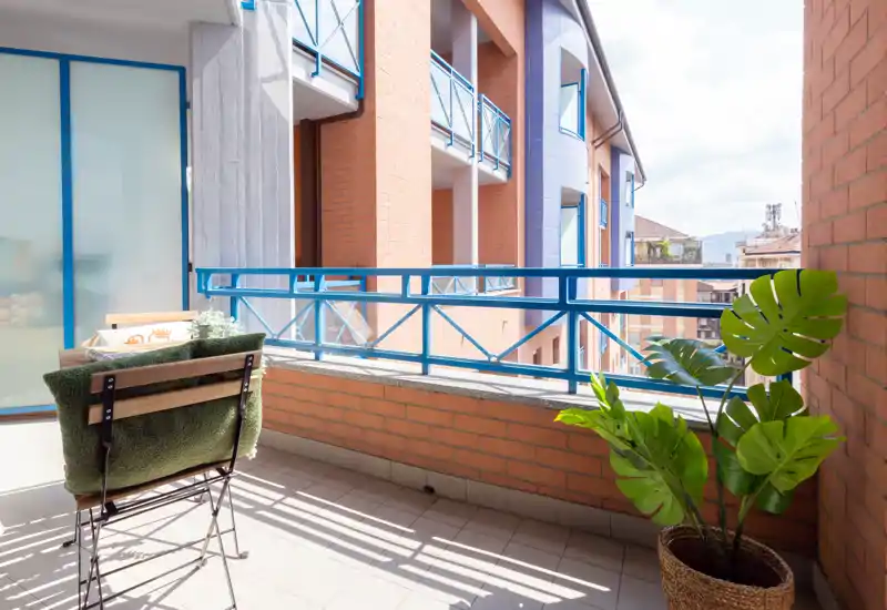 Sunny furnished balcony with a small chair, decorative cushion and potted plant overlooking neighboring terraces — ideal for morning coffee.