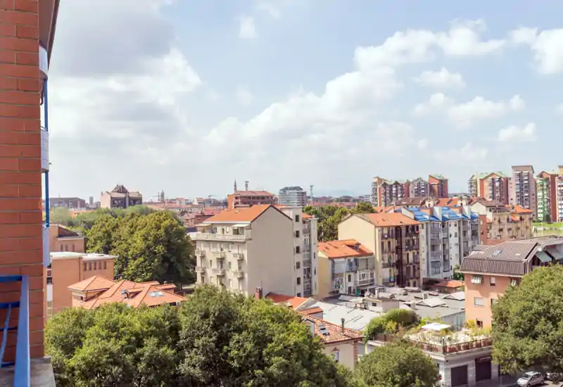 Sunny urban view from a balcony showing residential buildings, tree canopy and a clear sky—ideal for highlighting a terrace or balcony outlook.