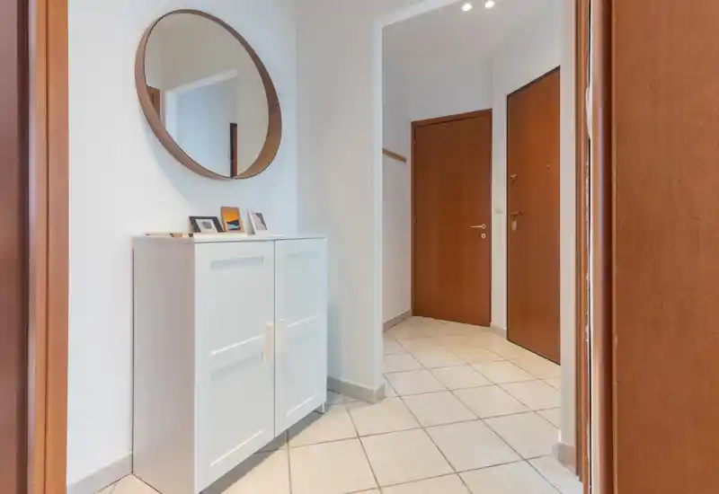 Neat, bright entrance hallway with tiled floor, white storage cabinet and a round wall mirror — ideal first impression for guests.