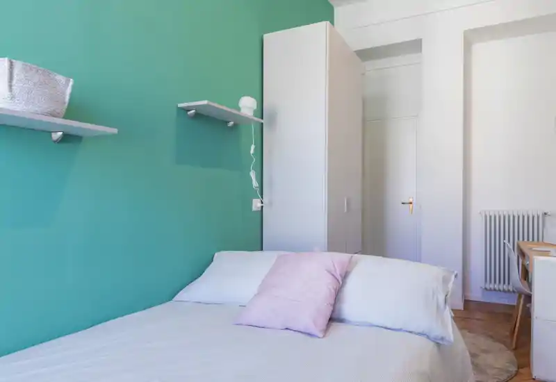 Chambre lumineuse et soignée avec un lit double devant un mur turquoise, une armoire et un petit bureau visibles — chaleureuse, propre et bien éclairée pour une annonce.
