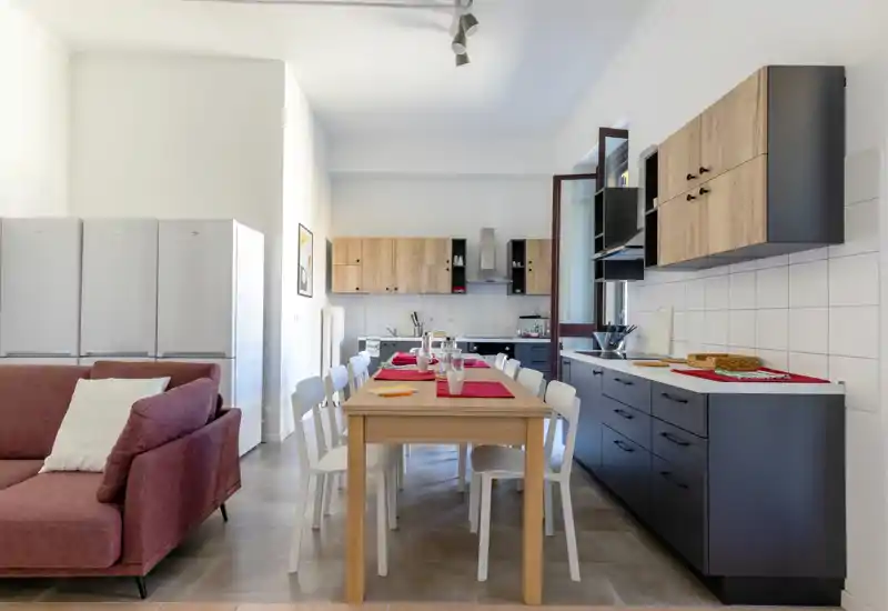 Cuisine moderne et lumineuse avec une table en bois centrale dressée pour des convives, des meubles bas foncés, des placards muraux en bois clair et un plan ouvert vers le séjour.