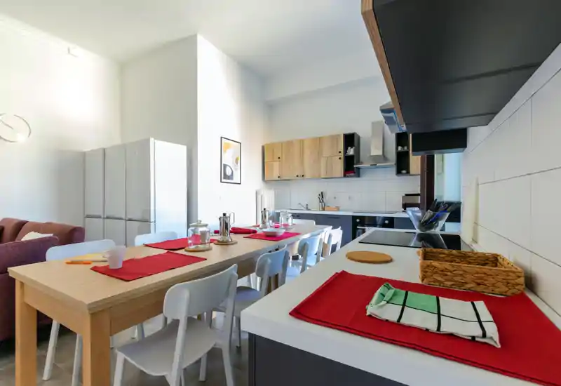 Cuisine ouverte avec une grande table dressée pour plusieurs convives ; meubles modernes, électroménagers et lumière naturelle claire créent un espace de cuisson et de repas accueillant.