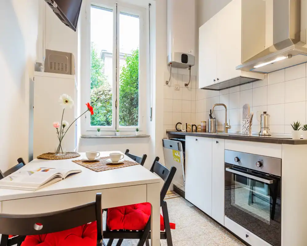 Cocina luminosa y bien decorada con mesa de comedor, horno moderno y una gran ventana que aporta luz natural — ideal para comidas cómodas y cocinar en casa.