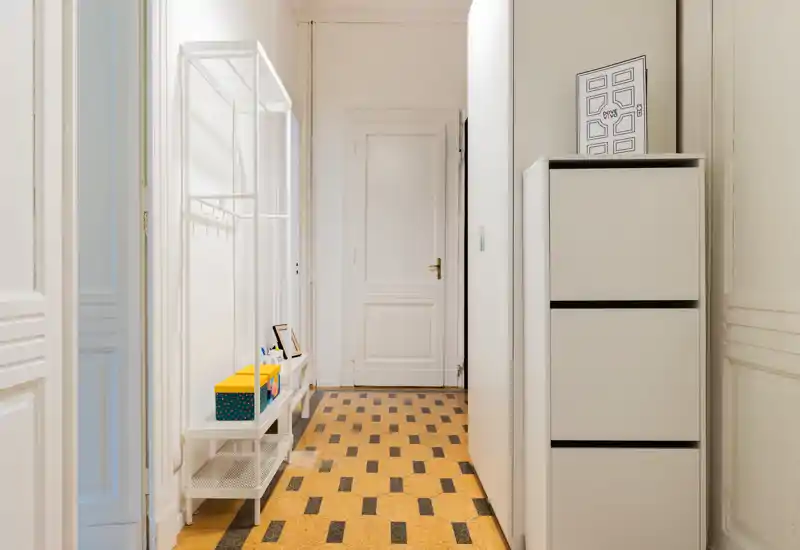 Bright, tidy entrance hallway with a slim shoe cabinet and open coat rack, patterned tiled floor and a white door at the end — ideal first impression for a flat listing.