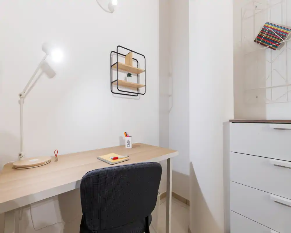 Rincón de oficina en casa luminoso y minimalista con escritorio de madera, lámpara de trabajo y silla cómoda — estantería y cómoda visibles, ideal para concentrarse.