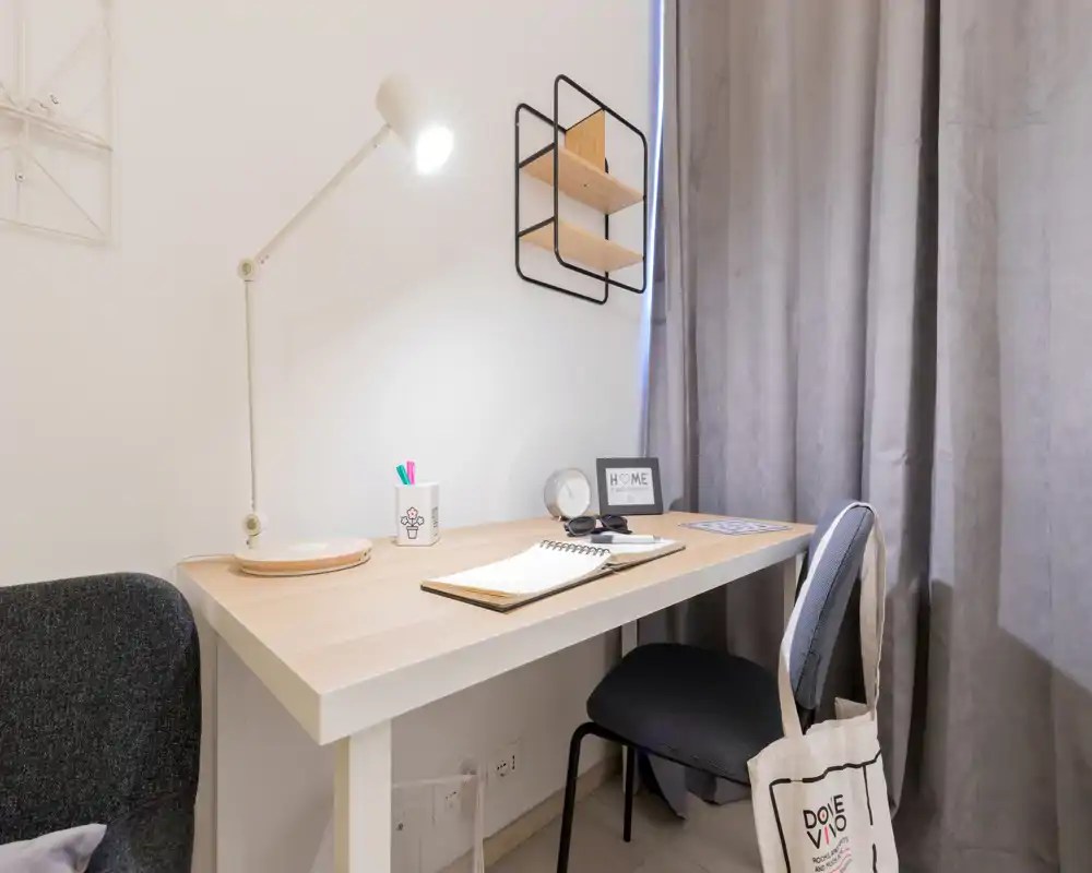 Compact, well-lit workspace corner with a wooden desk, adjustable lamp and chair — ideal for remote work or studying within the room.