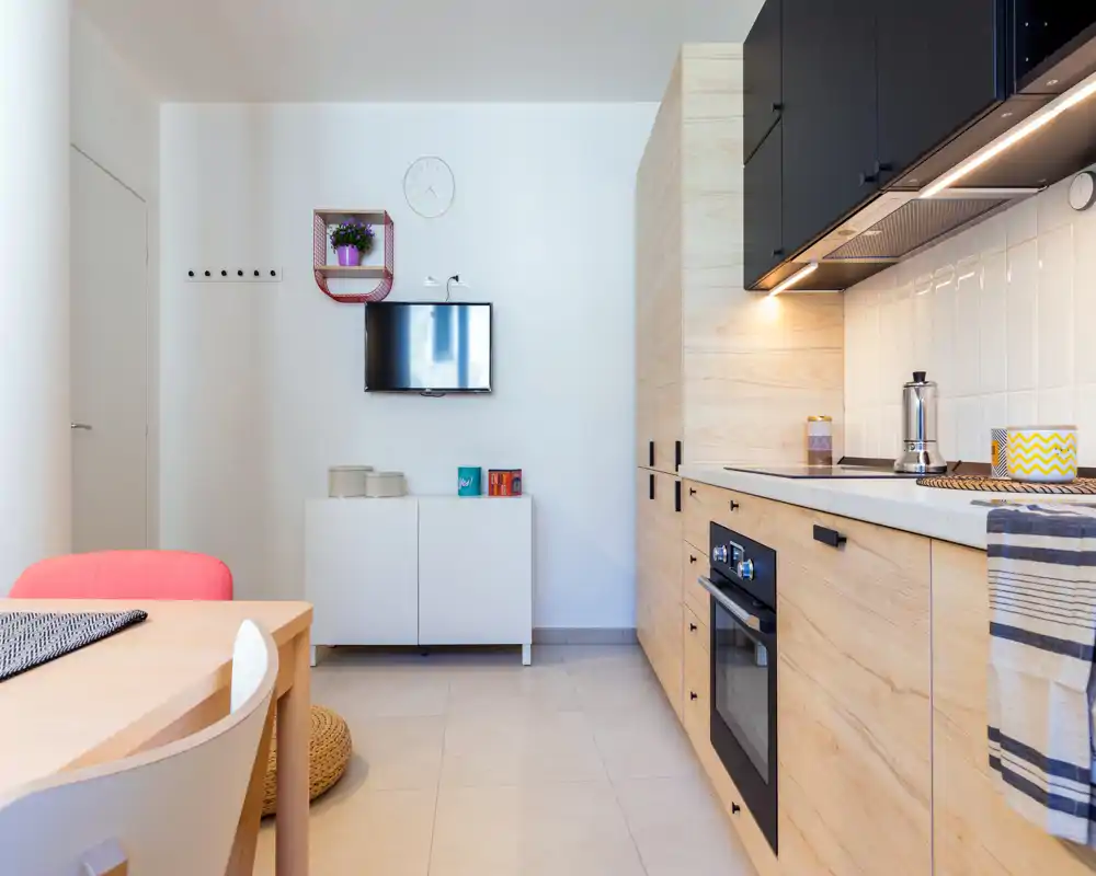 Bright, modern kitchenette with light wood cabinets, integrated oven and a small dining area — clean lines and cozy accents make it ideal for a compact rental.