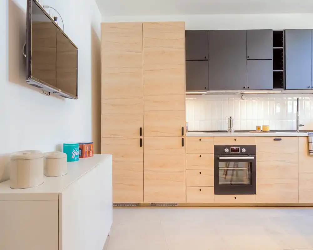 Modern kitchenette with warm wood cabinets, built-in oven and bright tiled backsplash — a compact, well-lit cooking area ideal for city apartments.