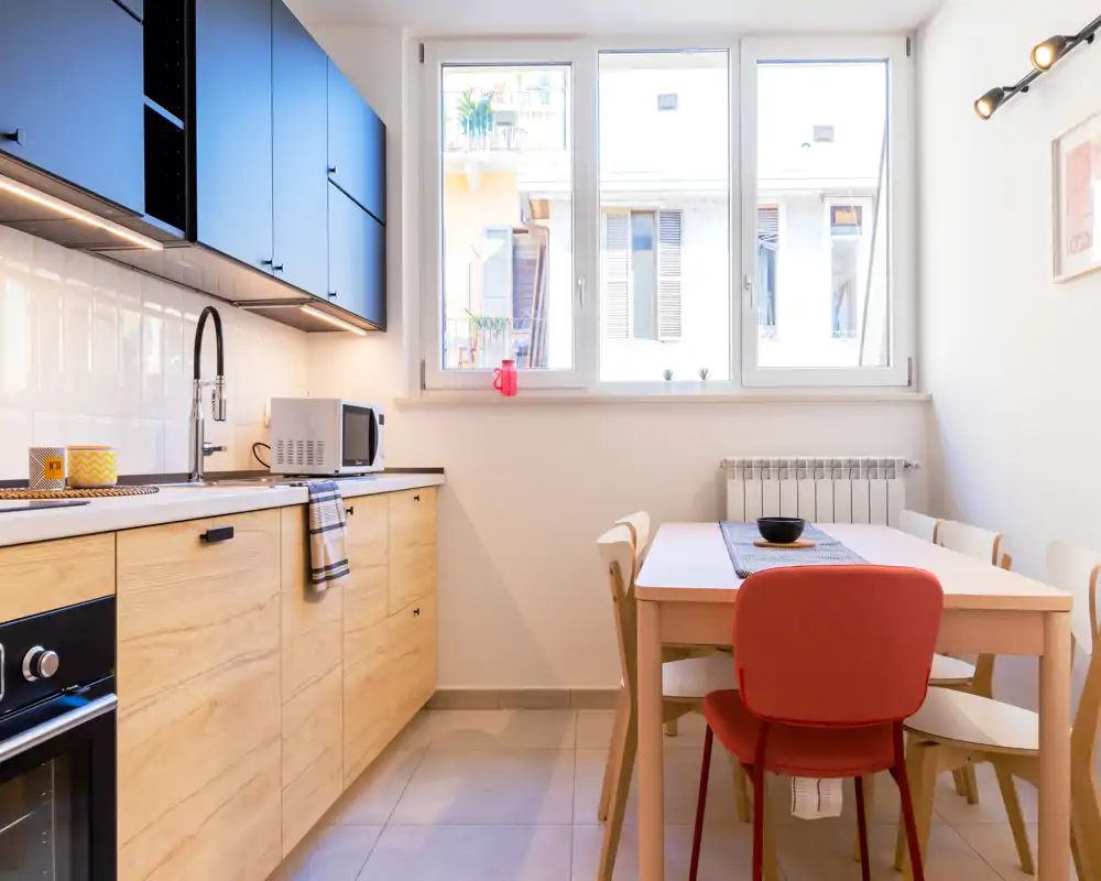 Modern fitted kitchen with light wood lower cabinets, dark upper cupboards and a small dining table by a large window. Bright, well-styled space ideal for compact apartment listings.