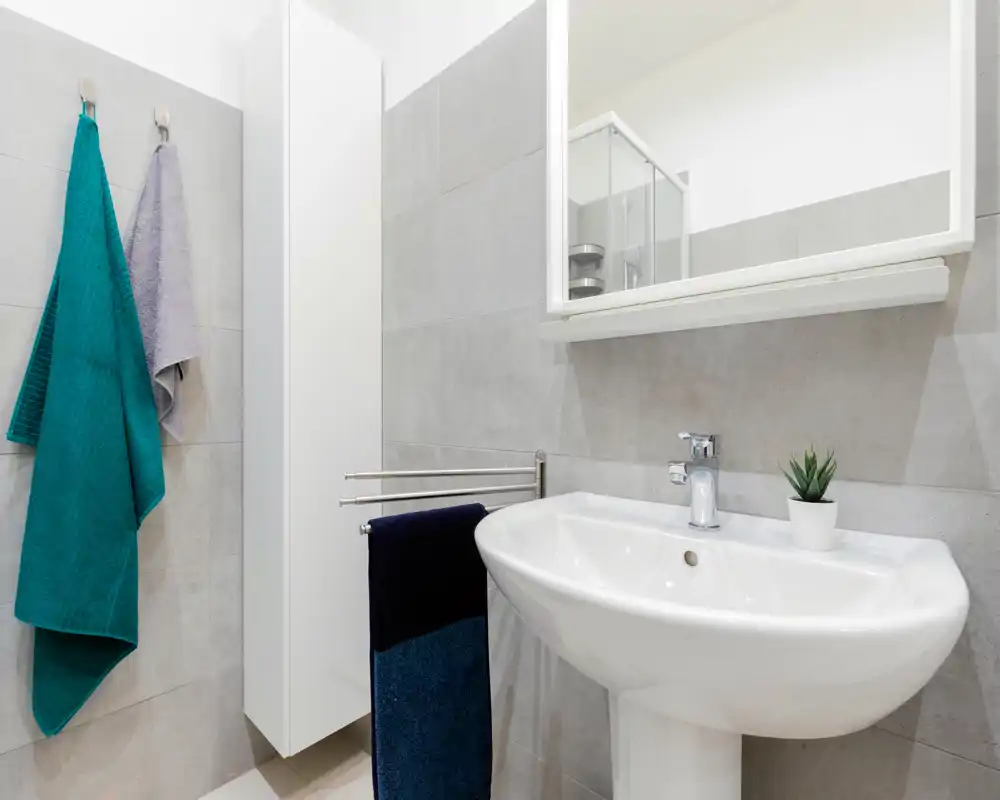 Bright, modern bathroom with a pedestal sink, mirror cabinet and neatly hung towels — clean, minimalist styling ideal for rentals.