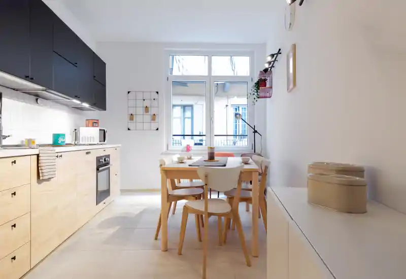 Bright modern kitchen with wood lower cabinets, black upper cabinetry and a small dining table set by a window — clean, well-lit and tastefully styled.