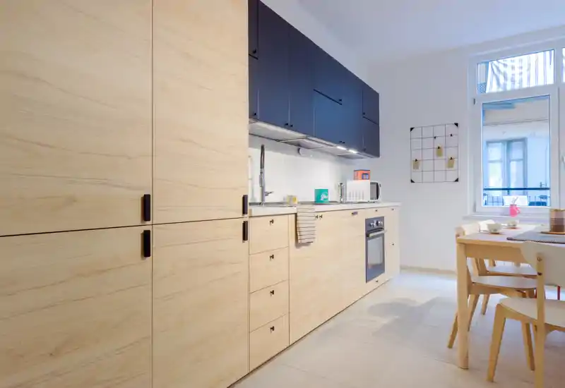 Bright modern kitchen with light wood cabinets, integrated appliances and a small dining table — clean, functional and welcoming.