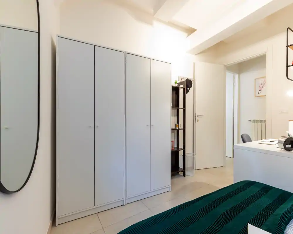 Dormitorio luminoso y ordenado con esquina de cama visible, gran armario y decoración minimalista — ideal para anuncios que destaquen el espacio y la luz.