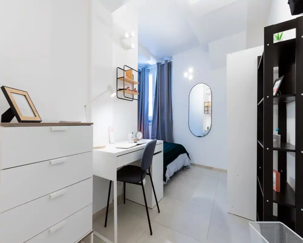 Dormitorio moderno y luminoso con cama individual, escritorio y almacenamiento; decorado para alquiler con tonos neutros y luz natural desde la ventana.
