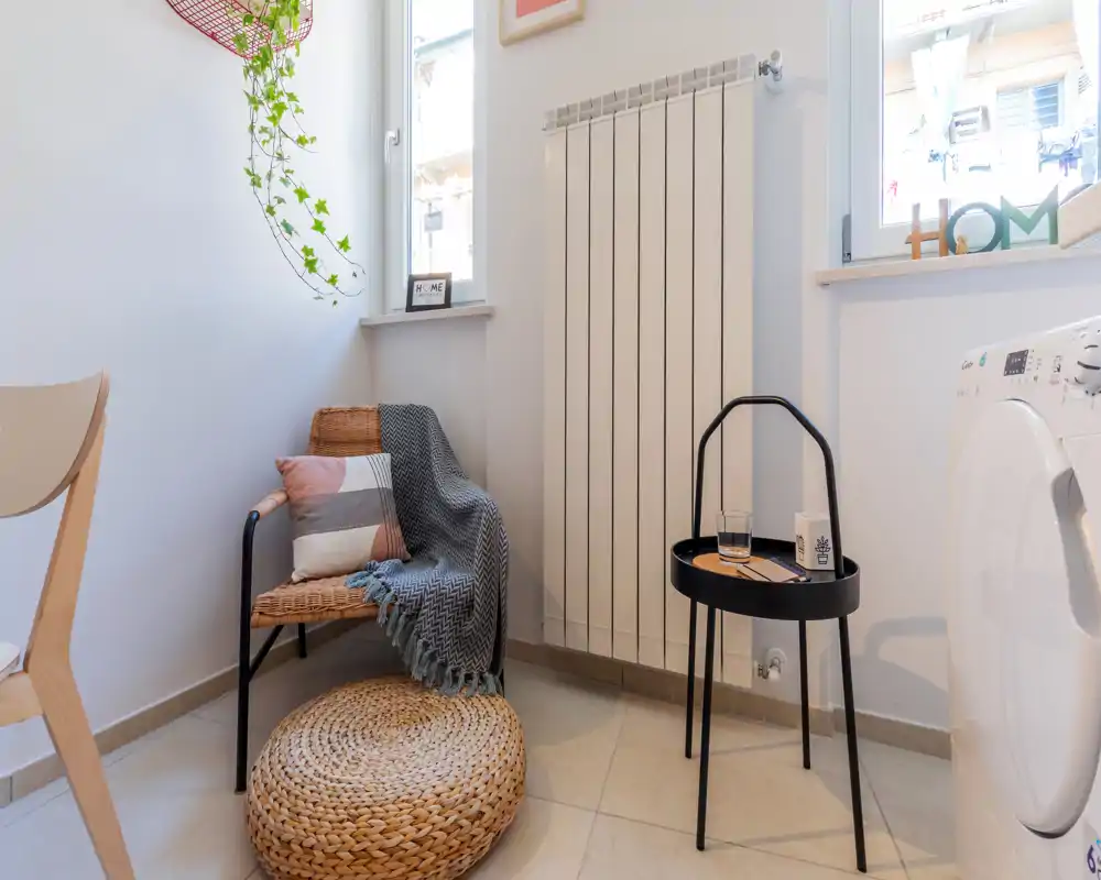 Rincón acogedor con silla de mimbre, puf trenzado y mesita auxiliar bajo luz natural, ideal para leer o relajarse. Paleta neutra y textiles suaves que generan una atmósfera cálida.