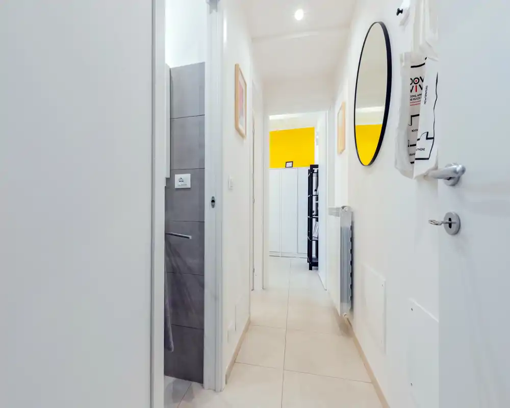 Entrada pasillo luminosa y moderna con suelo de baldosa, espejo en la pared y vista a las habitaciones contiguas. Estilo limpio y minimalista con buena iluminación, acogedor para los visitantes.
