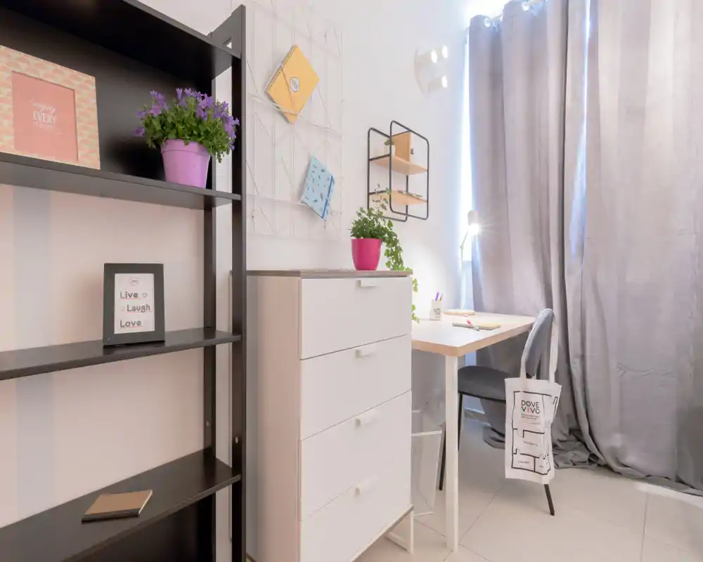 Rincón de dormitorio usado como zona de estudio: cómoda y escritorio de madera con silla junto a cortinas largas, estanterías decorativas y plantas que aportan calidez.