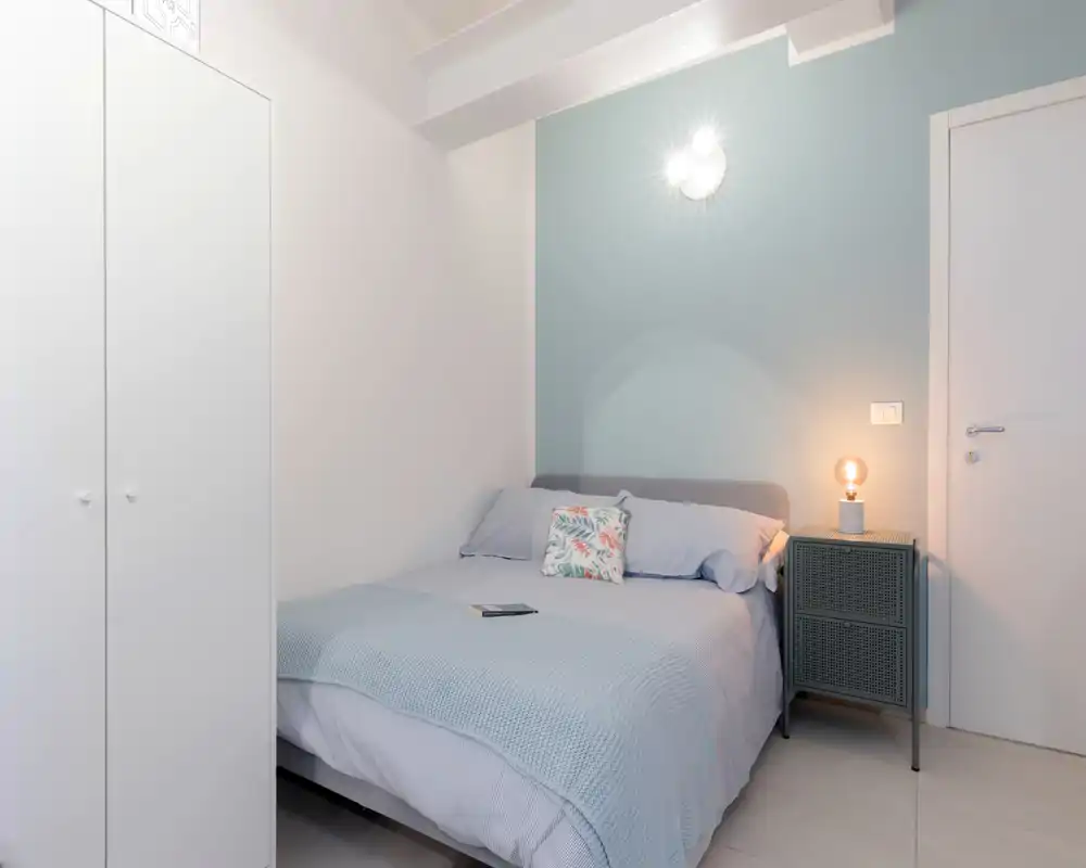 Dormitorio luminoso y acogedor con cama doble bien hecha, cojín decorativo y una mesita de noche con lámpara — perfecto para anuncios de alquiler.
