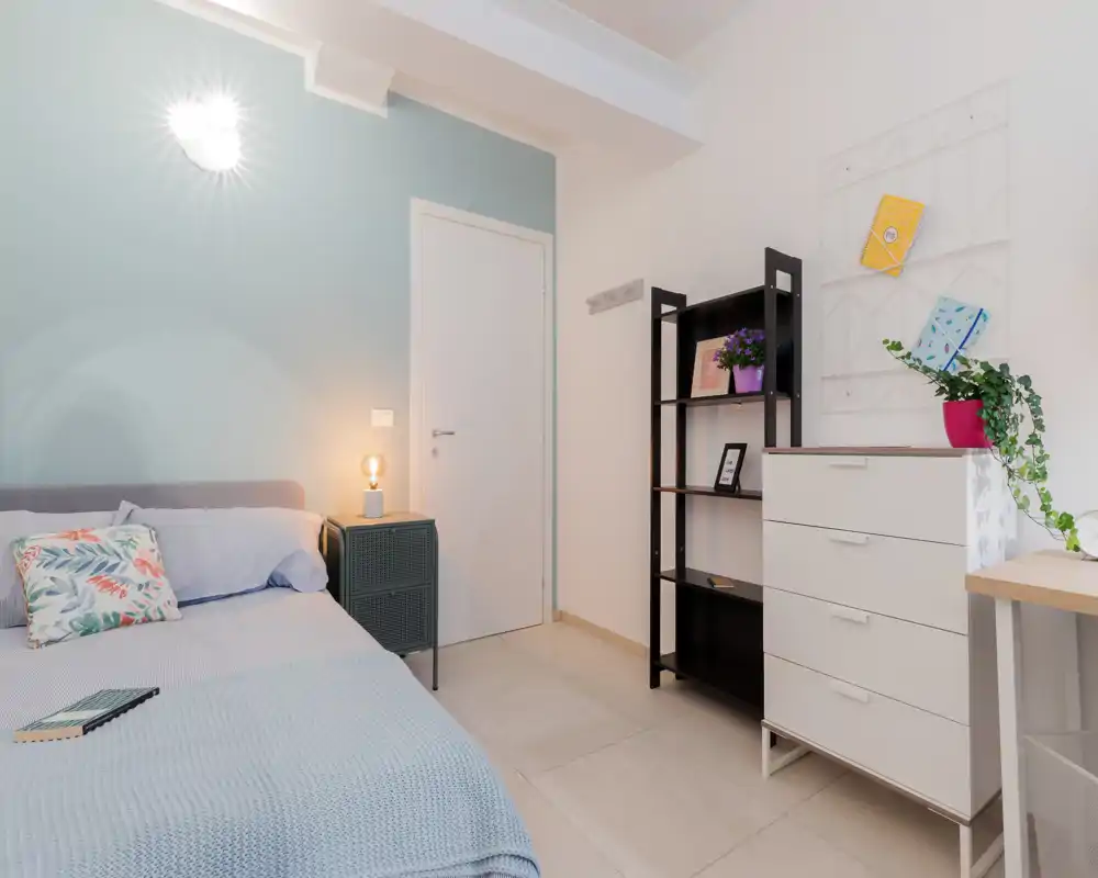 Dormitorio moderno y luminoso con cama bien hecha, pared en tonos pastel, lámpara de mesita y muebles ordenados — ideal para fotos de alquiler.