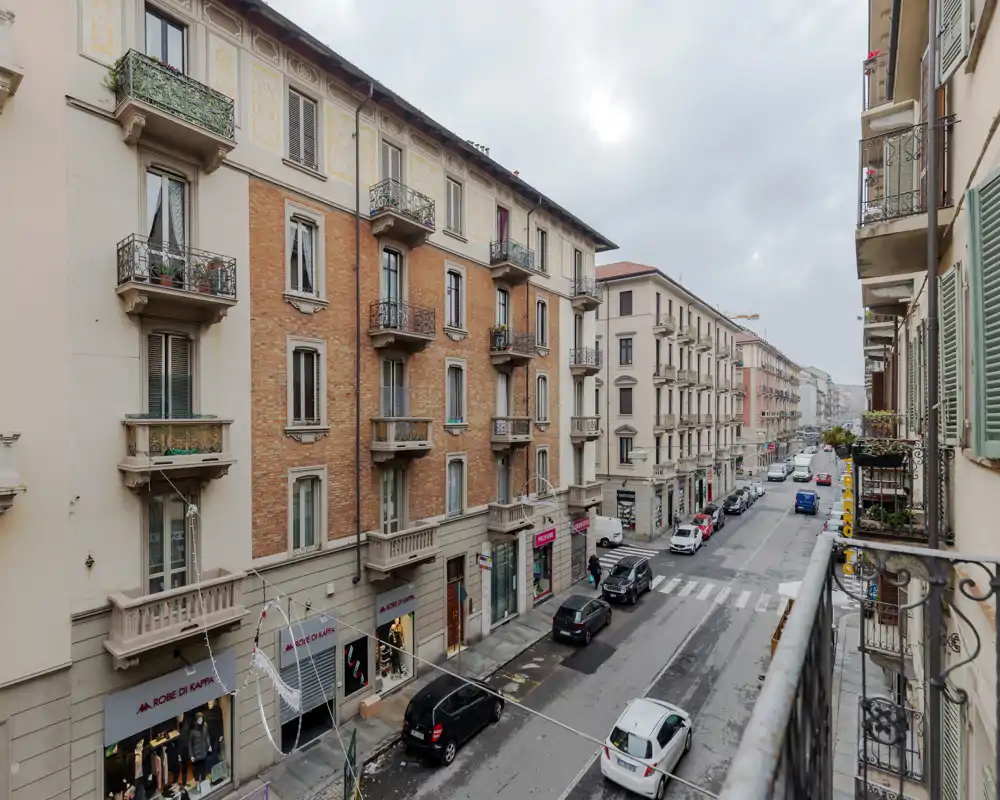 Balcony view overlooking a city street with classic apartment buildings, street-level shops and parked cars — ideal for highlighting location and street-facing aspects.