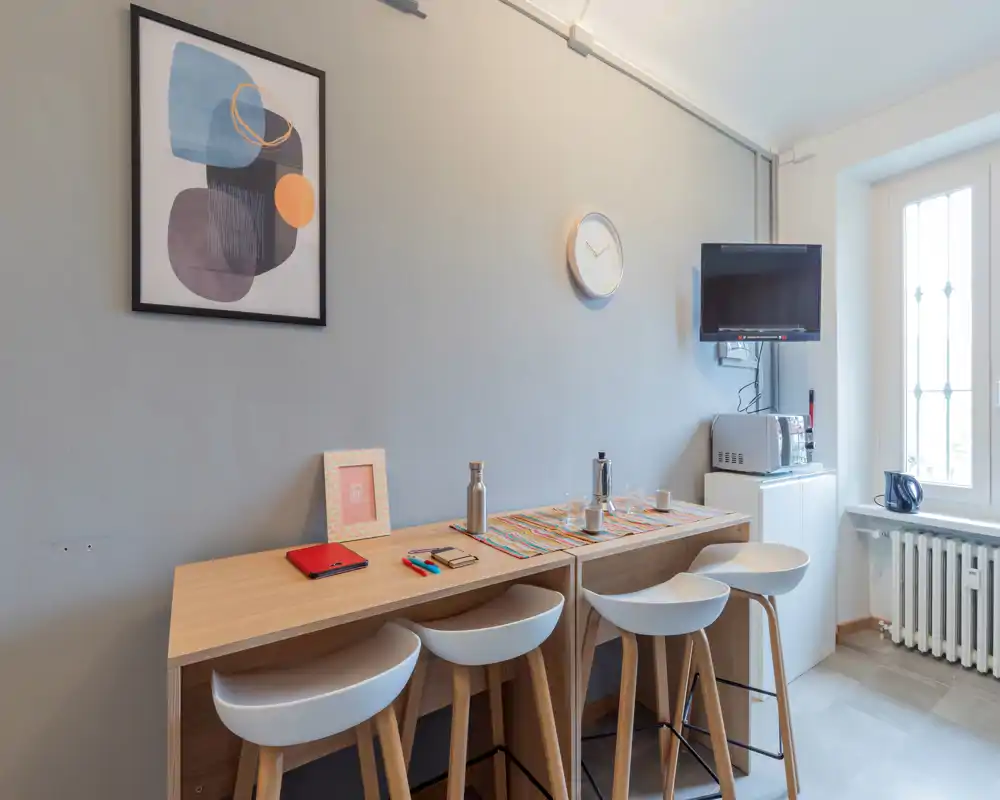 Stylish dining nook with a high wooden table and four modern bar stools, bright natural light from the window and tasteful wall decor — ideal for casual meals.