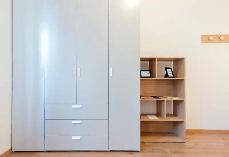Bright, minimal bedroom storage area with a large wardrobe and wooden shelving on a warm wood floor; clean, modern and uncluttered.