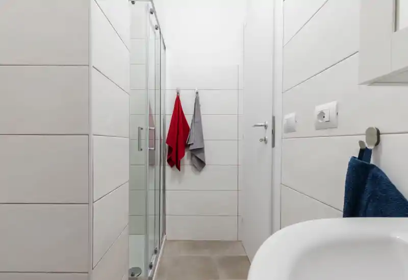 Compact modern bathroom with a glass shower enclosure, tiled walls and floor, and neatly hung towels. Clean, bright and minimal design ideal for rental listings.