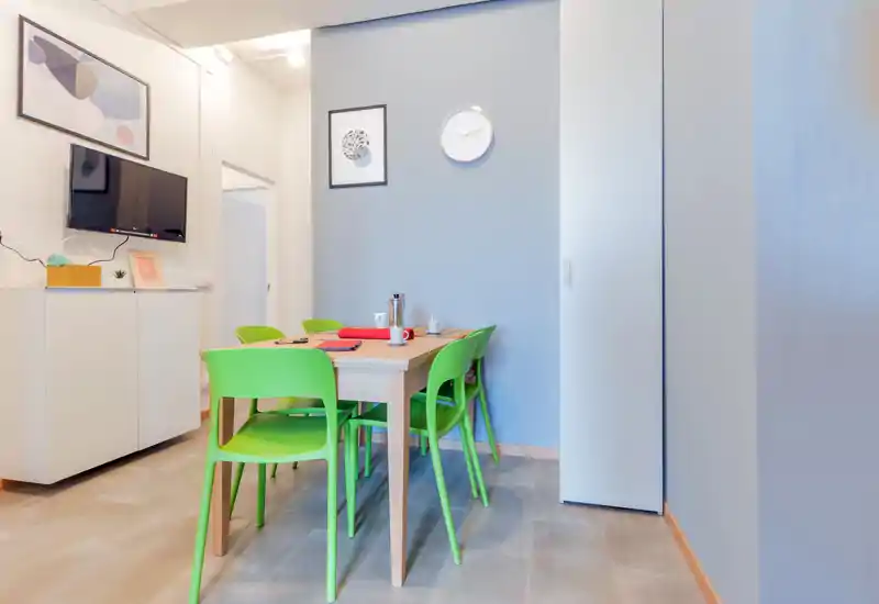 Bright, modern dining area with a wooden table and four vivid green chairs, simple wall art and a clean, minimal design ideal for casual meals.
