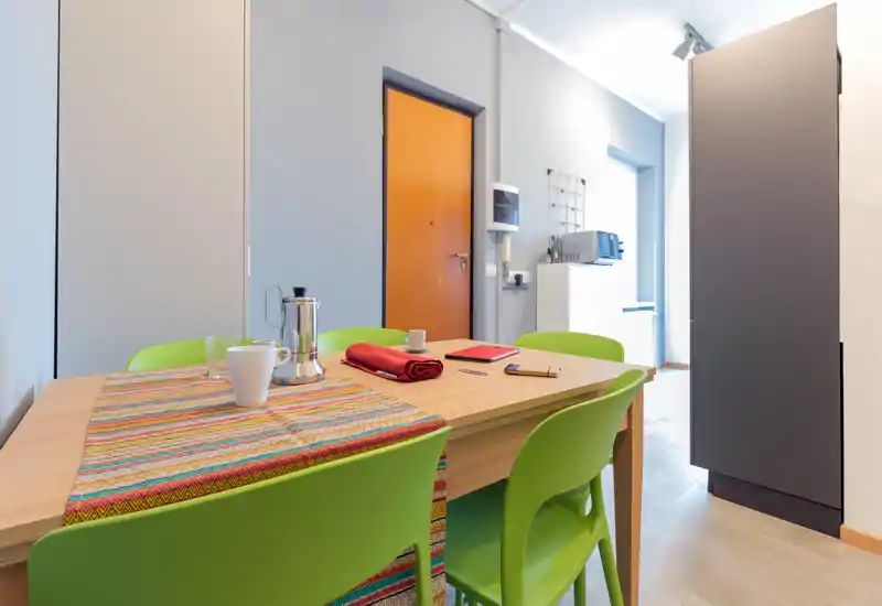 Well-lit dining area with a wooden table, colorful runner and four green chairs — modern, tidy and ready for meals.