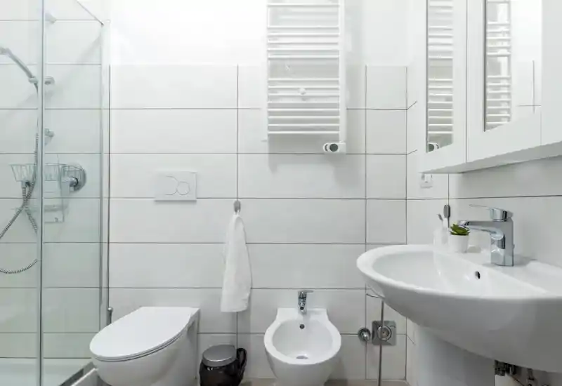 Bright, modern bathroom with a shower enclosure, toilet, bidet and a wall-mounted sink with mirror storage. Clean white tiles and chrome fixtures create a fresh, minimal look.