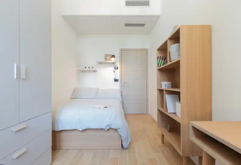 Dormitorio luminoso y minimalista con cama doble bien hecha, muebles de madera clara y tonos neutros que crean un ambiente tranquilo y acogedor.