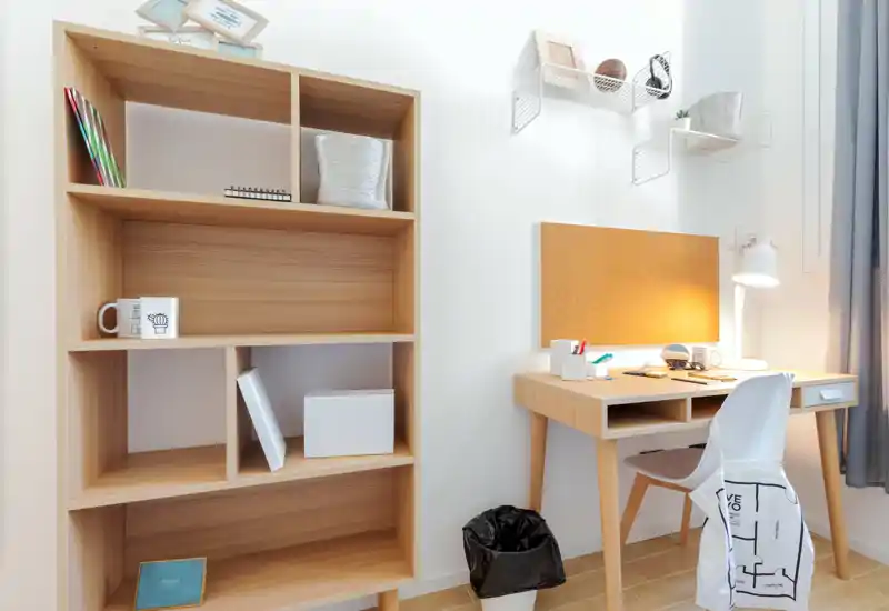 Bright, modern small home office corner with a wooden desk, task lamp, cork board and shelving — a neat workspace ideal for study or remote work.