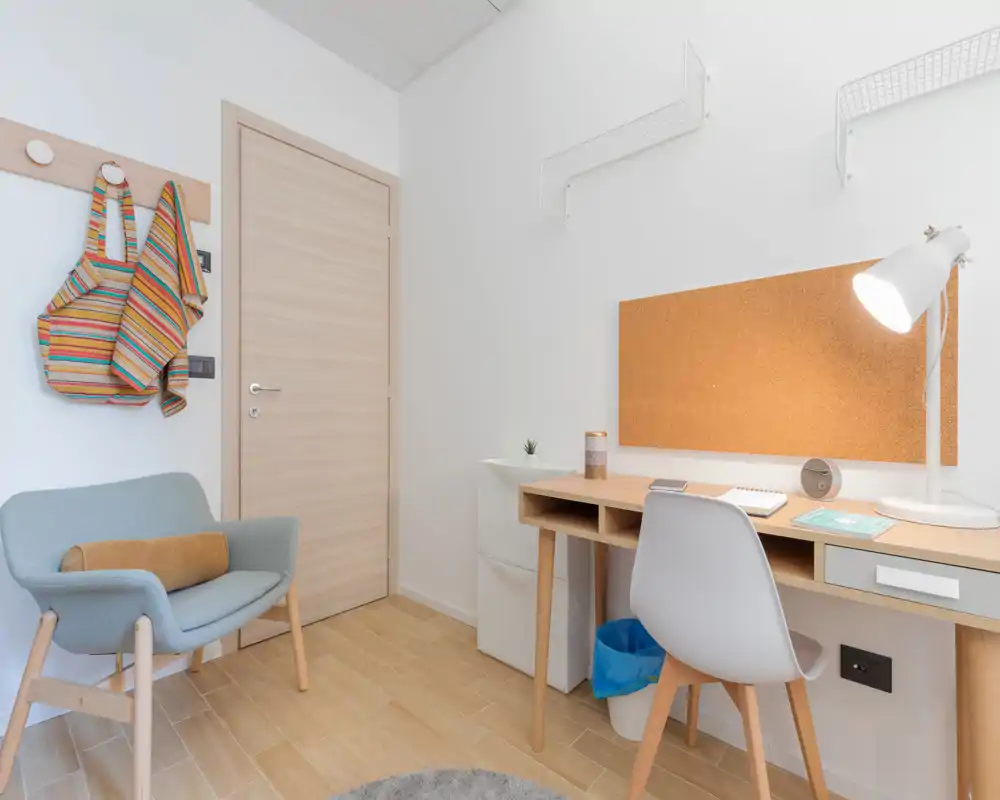 Bright, modern living area with a compact work desk, cork pinboard and a comfortable armchair — ideal for a home office corner in a small apartment.