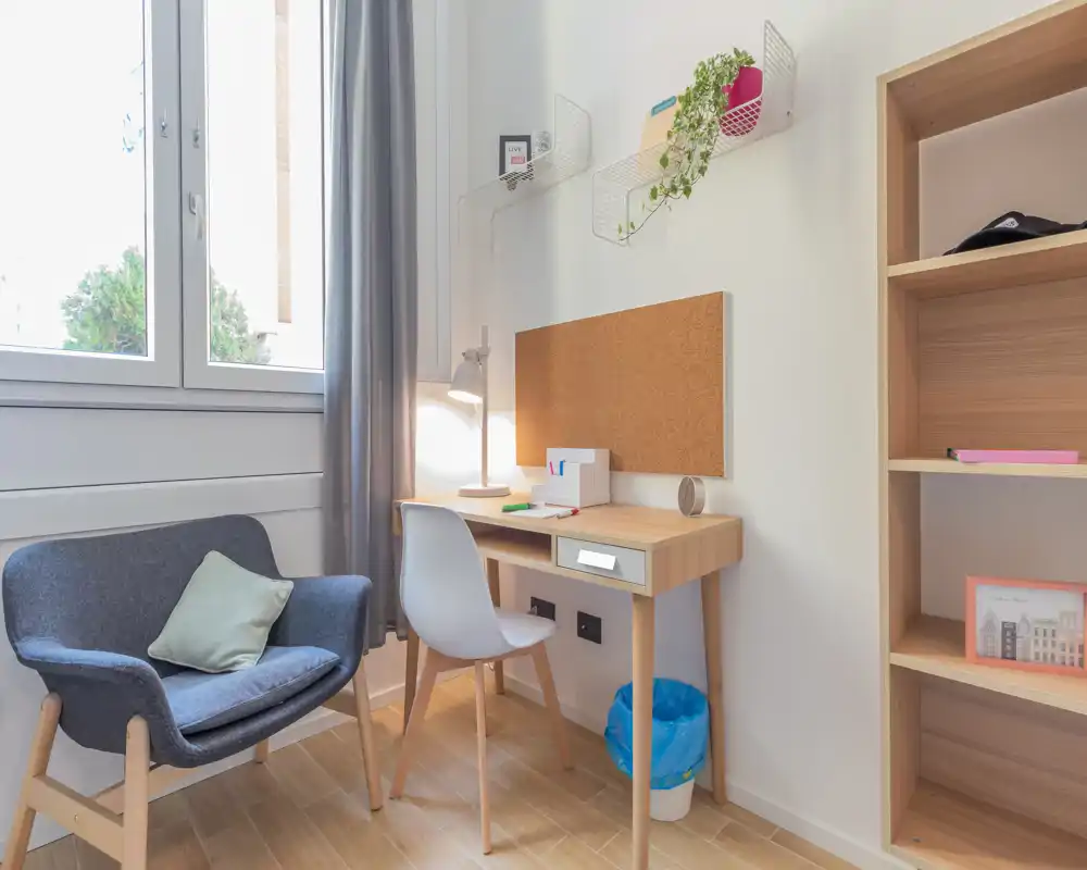 Coin salon lumineux et accueillant avec un fauteuil confortable, un petit bureau et des étagères — idéal pour se détendre ou travailler près de la fenêtre.
