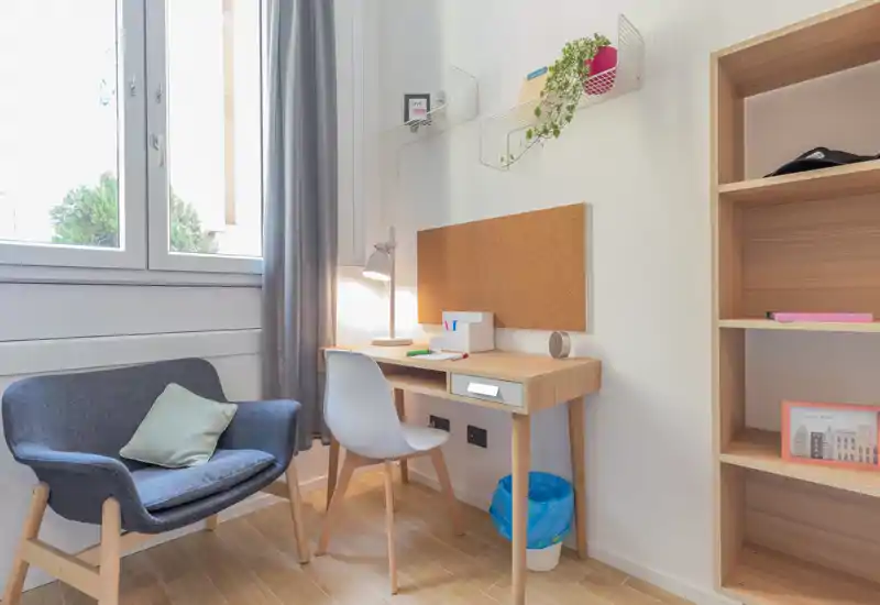 Bright, cozy living corner with a comfortable armchair, a compact desk and shelving — ideal for relaxing or working by the window.