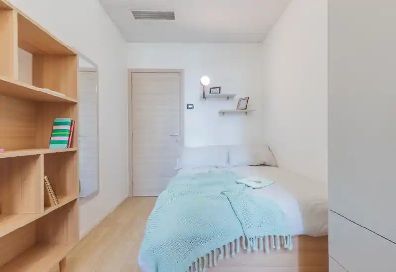 Chambre lumineuse et compacte avec un lit double confortable, des coussins moelleux et un plaid en maille. Des étagères en bois et une décoration minimaliste créent une atmosphère moderne et apaisante, parfaite pour la location saisonnière.
