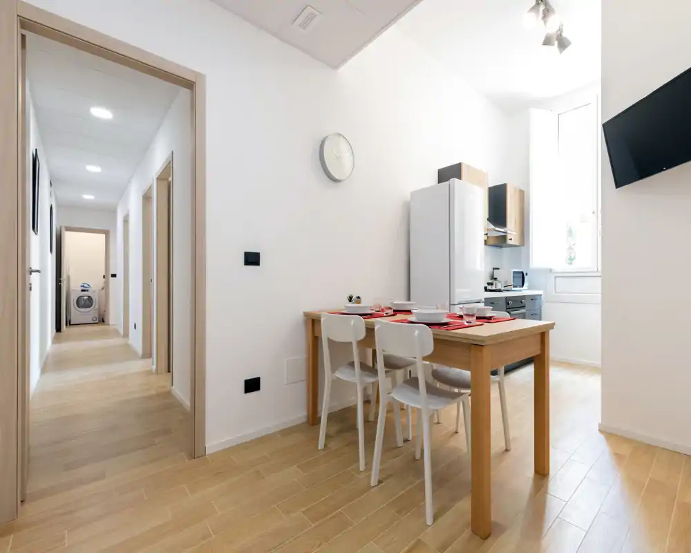 Espace repas moderne et lumineux relié à une petite cuisine — table en bois pour quatre, chaises blanches et grande fenêtre apportant une belle lumière naturelle.