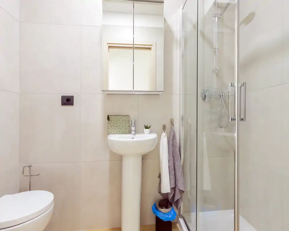 Salle de bain moderne et lumineuse avec lavabo sur colonne, armoire-miroir, cabine de douche vitrée et WC mural ; carrelage neutre et accessoires soignés.