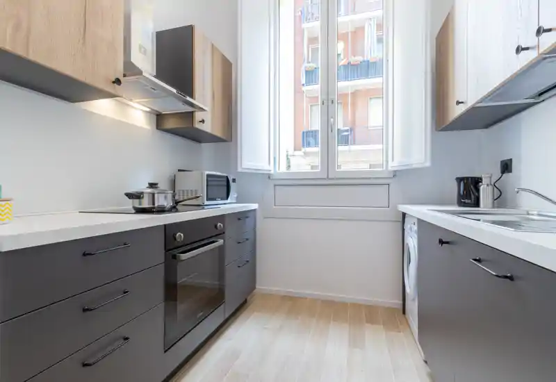 Bright, modern kitchen with built-in oven, induction hob, microwave and a large window providing ample natural light; sleek cabinets and wood-effect flooring create a clean, welcoming space.