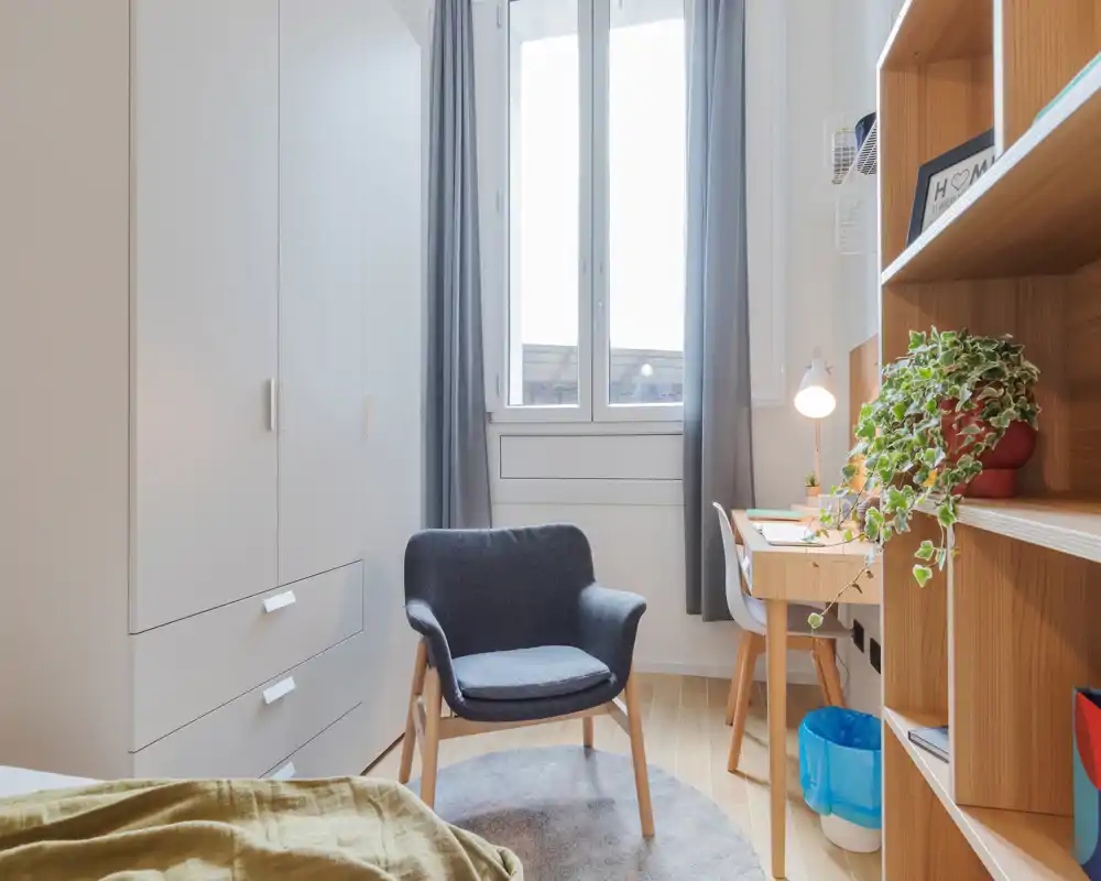 Rincón de dormitorio luminoso y acogedor con un sillón cómodo, armario empotrado y escritorio junto a la ventana: ideal para relajarse o trabajar.