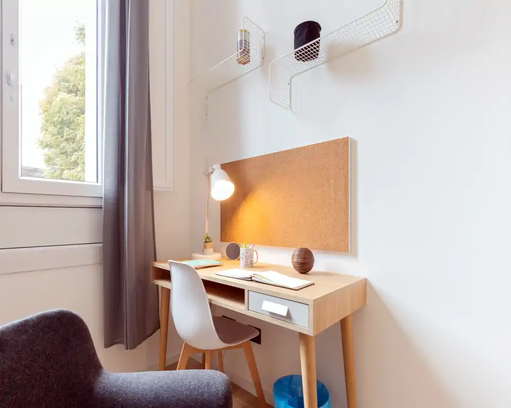 Zona de estar luminosa y acogedora con un escritorio de madera compacto y un sillón de lectura: un rincón de trabajo cómodo junto a la ventana con luz cálida.